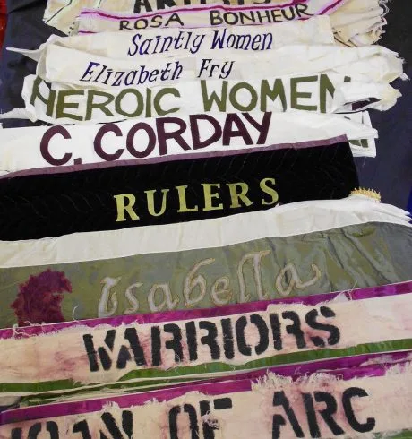 Suffragette banners in white, green and purple are decorated with the names and occupations of feminist heroes