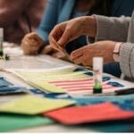 The hands of two people can be seen at a table using colourful materials to work on craft activities.