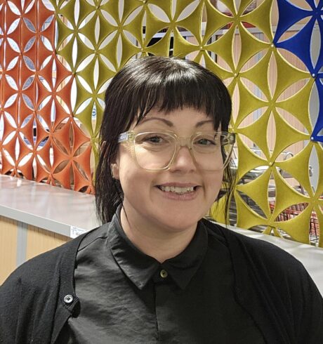 Xana Marwick, Luminate's Administrative Officer, wearing a black shirt and standing in front of a colourful room divider.