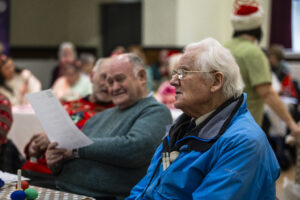 Two men in the foreground with other people behind hold song sheets
