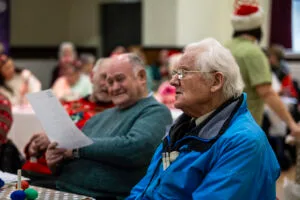 Two men in the foreground with other people behind hold song sheets