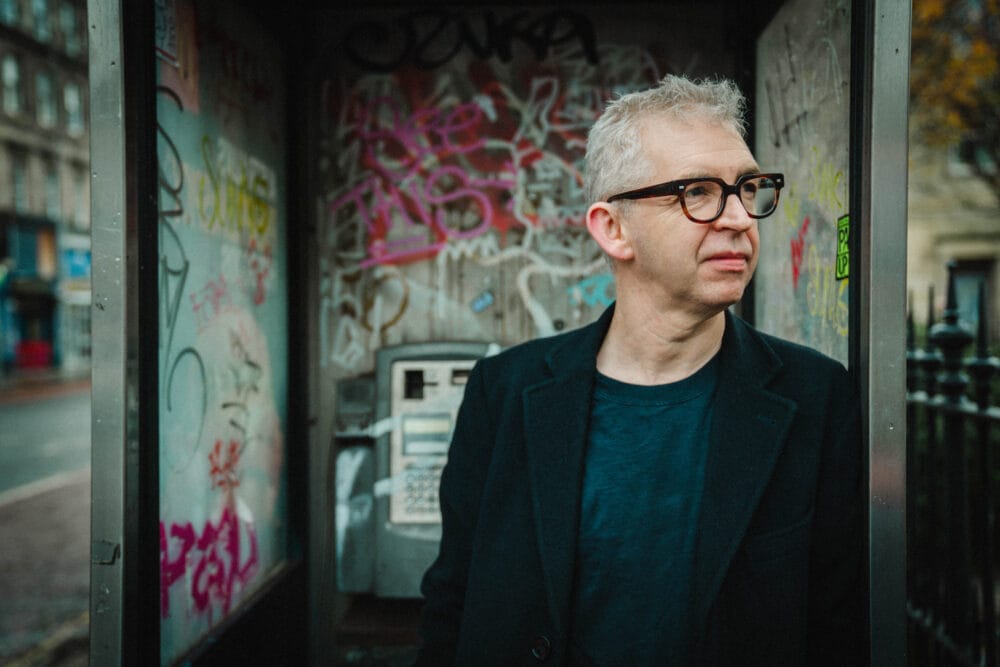 Photograph of Stephen Deazley standing in front of a phone box with graffiti.
