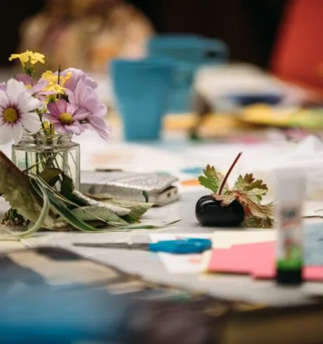 Craft materials and a small vase of flowers sit on a table.