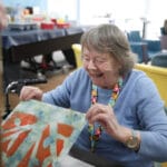 An older woman in a blue sweater smiles and looks at her newly created screenprint