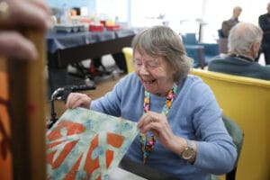 An older woman in a blue sweater smiles and looks at her newly created screenprint