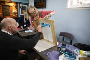 Artist assisting a man to do a screenprint.