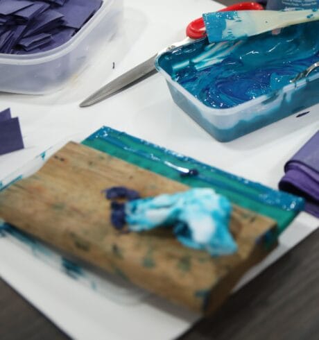 Art materials including trays of paint, tissue paper and scissors on a table.