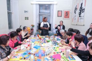 Participants at an art workshop seated around a table covered in art materials