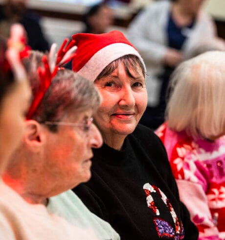 A group of women wearing festive clothing. A woman in a red Santa hat smiles at the camera.