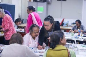Women at tables in a community centre doing art activities