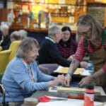 An artist helps a seated woman do screenprinting at Lochside Connections Meeting Centre.