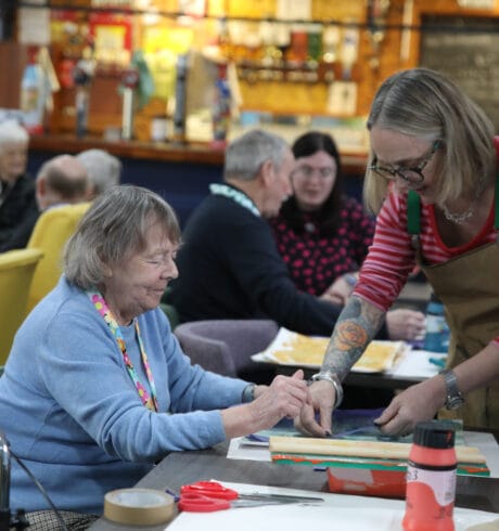 An artist helps a seated woman do screenprinting at Lochside Connections Meeting Centre.