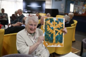 A woman holds up at artwork she has created at Lochside Connections Meeting Centre.